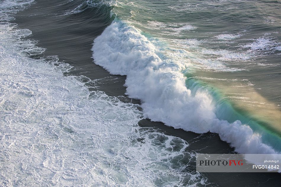 The sun at sunset, illuminates the waves crashing against the cliffs of Capo Nieddu