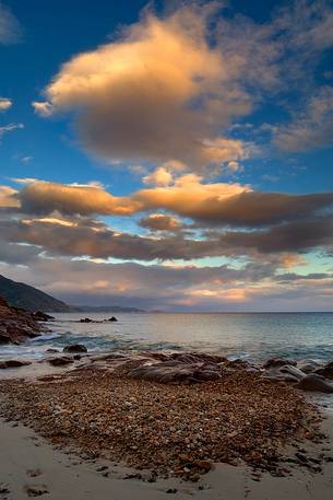 A small bay near the port of Teulada illuminated by the last rays of sun. The clouds are the mirror to the bathroom dry pebbles, while the dusk gives way to the colors of the sunset, Teulada, Sulcis-Iglesiente, Sardinia, Italy