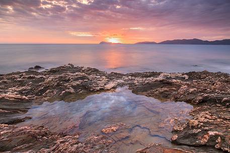 The colors of the rocks of the Piscinn bay appear lit from the sun on the horizon, giving unusual and attractive colors