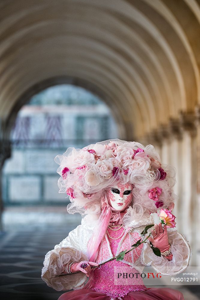 Woman wearing carnival mask and costume under Doge's Palace colonnade, Piazza San Marco or St Mark's Square, Venice, Italy, Europe