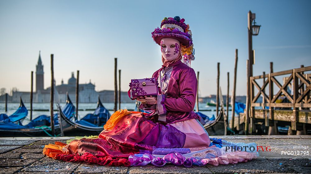 Carnival mask in the San Marco square with gondolas moored in the San Marco basin and the San Giorgio Maggiore church in the background, Venice, Italy, Europe