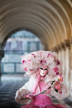 Woman wearing carnival mask and costume under Doge's Palace colonnade, Piazza San Marco or St Mark's Square, Venice, Italy, Europe