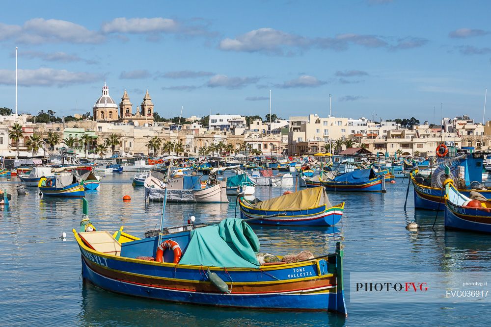 The historic city of Marsaxlokk on the island of Malta, famous for its colorful fishing boats called Iuzzu, in the background the Parish church dedicated to Our Lady of Pompeii, Malta, Europe