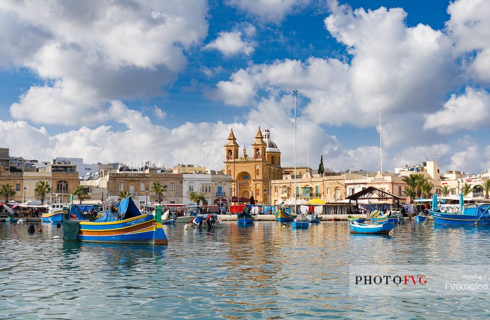 The historic city of Marsaxlokk on the island of Malta, famous for its colorful fishing boats called Iuzzu, in the background the Parish church dedicated to Our Lady of Pompeii, Malta, Europe