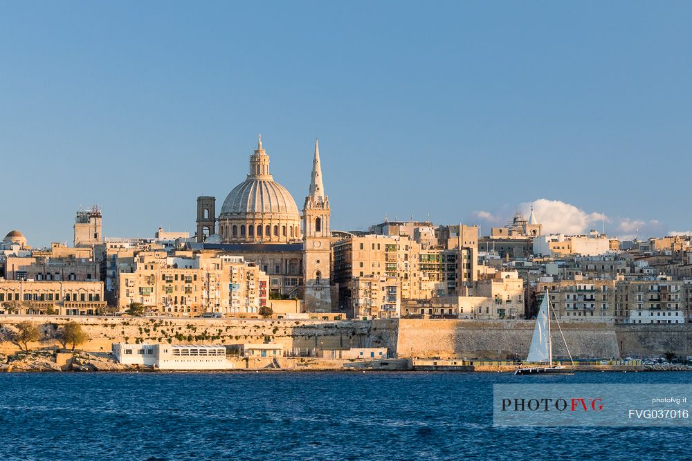 Panoramic view of Saint Paul's Cathedral and the ancient walls of Valletta with sail boat at the sunset, Malta, Europe