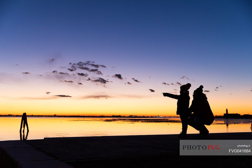 Silhouette of mother and child at twilight and in the background the island of Venice, from Burano island, Venetian lagoon, Veneto, Italy, Europe