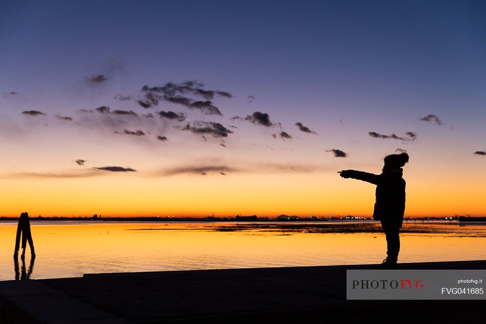 Child in silhouette at twilight with Venice in the background, from Burano island, Venetian lagoon, Veneto, Italy, Europe