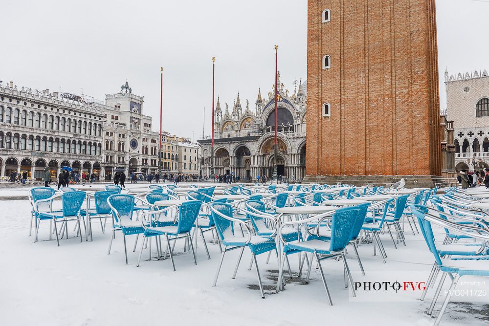 Snowy chairs on Piazza San Marco or St Mark square and in the background the Basilica of San Marco church with bell tower and the Doge Palace, Venice, Italy