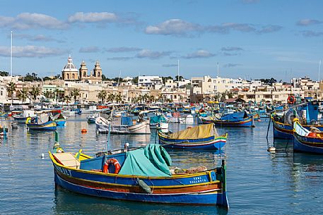 The historic city of Marsaxlokk on the island of Malta, famous for its colorful fishing boats called Iuzzu, in the background the Parish church dedicated to Our Lady of Pompeii, Malta, Europe