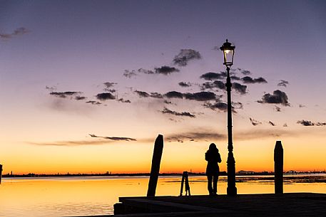 Woman in silhouette at twilight looking Venice island from Burano island, Venetian lagoon, Veneto, Italy, Europe Woman in silhouette at twilight looking Venice island from Burano island, Venetian lagoon, Veneto, Italy, Europe