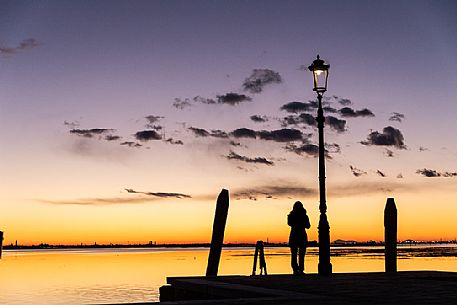 Woman in silhouette at twilight looking Venice island from Burano island, Venetian lagoon, Veneto, Italy, Europe