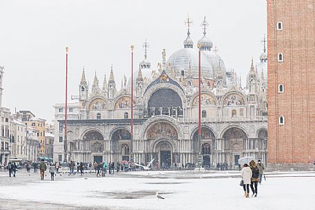 Tourists on Piazza San Marco or St Mark square and in the background the Basilica of San Marco church with bell tower in a snowy day, Venice, Italy