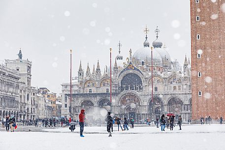 Tourists on Piazza San Marco or St Mark square and in the background the Basilica of San Marco church with bell tower in a snowy day, Venice, Italy