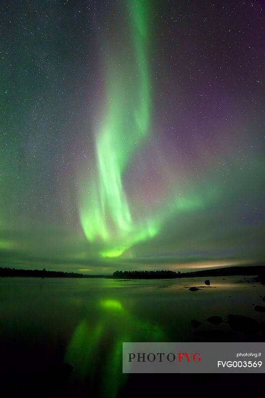 Northern lights over finnish Lapland reflected on the river between Sweden and Finland.