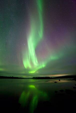Northern lights over finnish Lapland reflected on the river between Sweden and Finland.