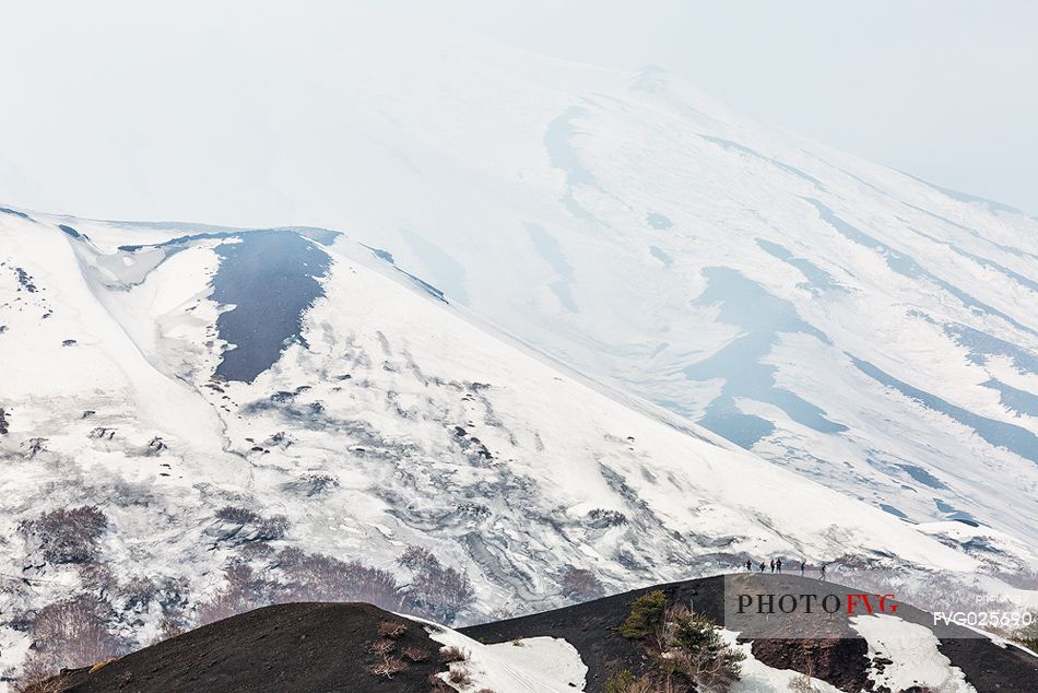 Tourists walking in foggy morning, in the background the Etna volcano from Sartorius mountais, Sicily, Italia