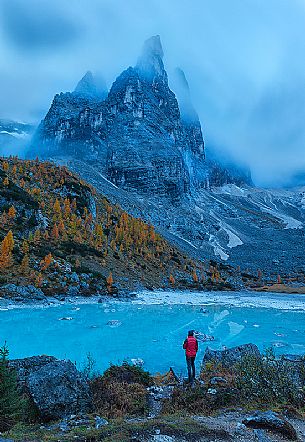 Hiker admires the magic light blue of Sorapis glacial Lake in autumn sorrounded by pine and yellow larches, Cortina d'Ampezzo, dolomites, Italy