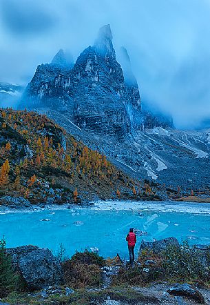 Hiker admires the magic light blue of Sorapis glacial Lake in autumn sorrounded by pine and yellow larches, Cortina d'Ampezzo, dolomites, Italy Hiker admires the magic light blue of Sorapis glacial Lake in autumn sorrounded by pine and yellow larches, Cortina d'Ampezzo, dolomites, Italy