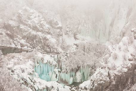 Tourists admiring frozen lakes and waterfalls in Plitvice Lakes National Park, Croatia