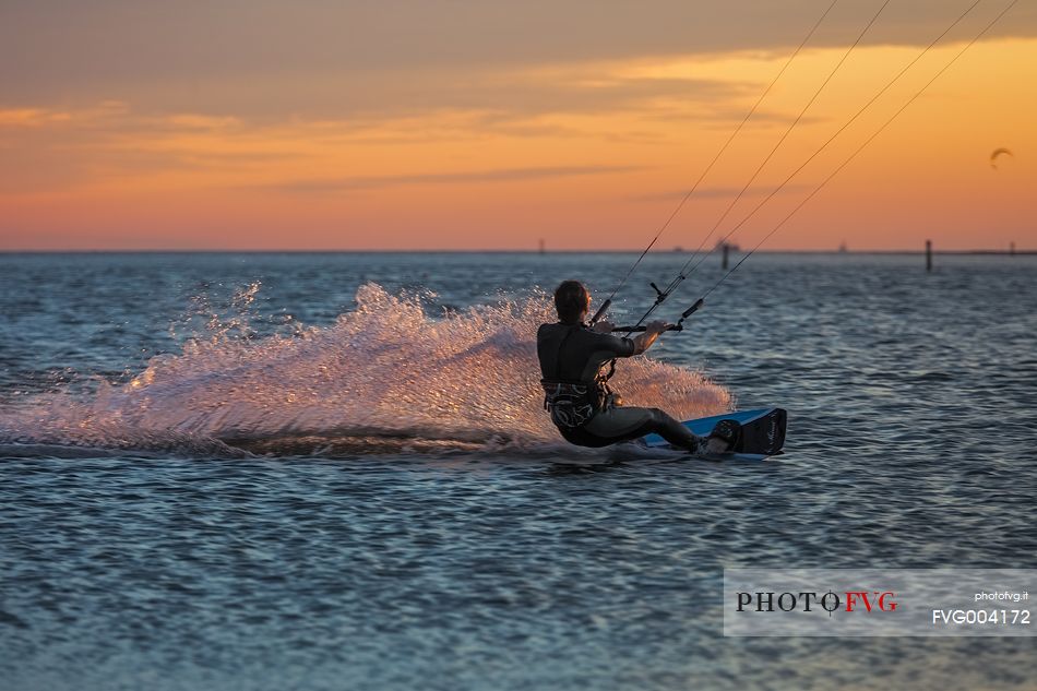 Kitesurfing running fast at sunset in the lagoon of Grado