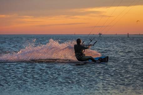 Kitesurfing running fast at sunset in the lagoon of Grado