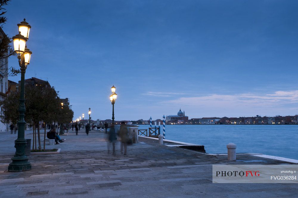 Tourists walk on the foundations of the Zattere in the Dorsoduro district of Venice. On the background the church of the Redentore or Redeemer on the Giudecca island, Italy.