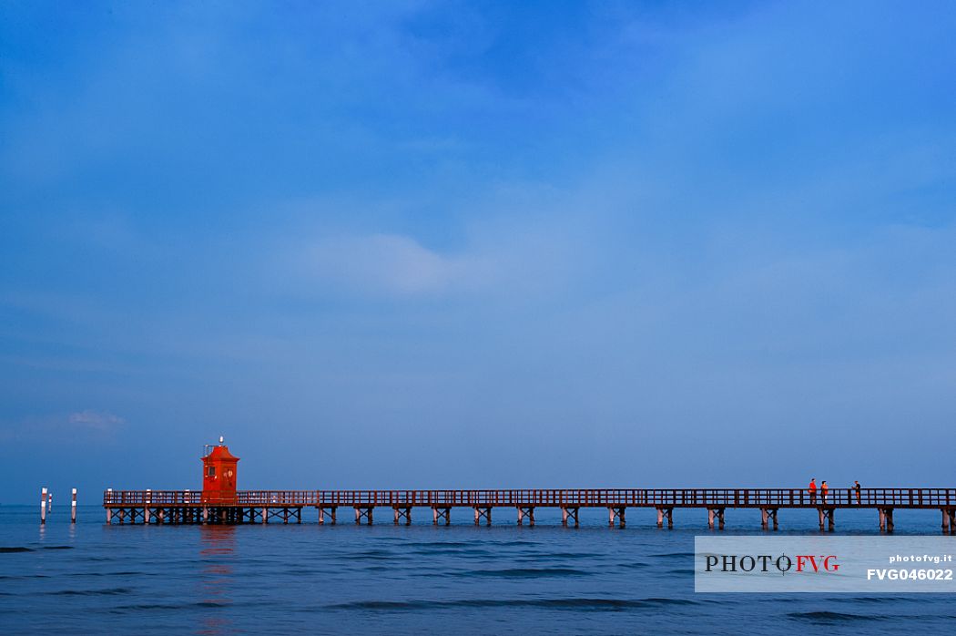 Tourists on the pier of Punta Faro lighthouse in Lignano Sabbiadoro at sunset, a beautiful seaside resort in Friuli Venezia Giulia, Italy, Europe