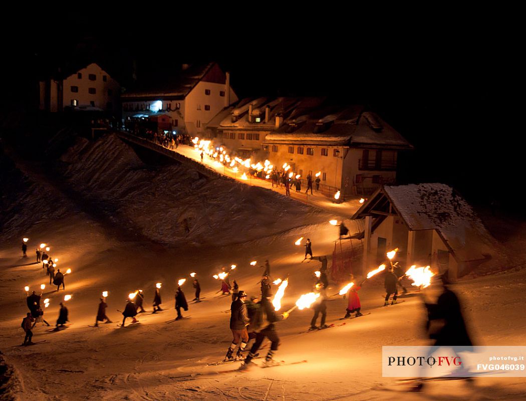 Costumed skiers descend from Monte Lussari mount with the torch lit on New Year's day. Tarvisio, Julian alps, Friuli Venezia Giulia, Italy, Europe
