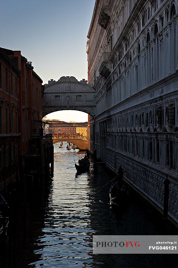 Gondoliers on the Rio di Palazzo show tourists the famous Bridge of Sighs or Ponte dei Sospiri, in the background illuminated by the morning light the Ponte della Paglia. Venice, Italy, Europe