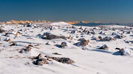 Rocks emerge from the blanket of snow, in the background  the Julian Alps, Piancavallo, Friuli Venezia Giulia, Italy