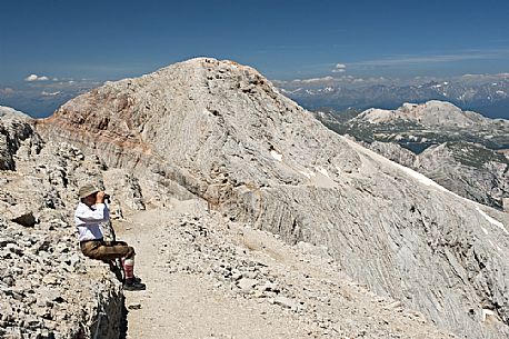 A man in mountain clothes watches the dolomites by binoculars, Cima Tofana peak, Cortina d'ampezzo, Italy