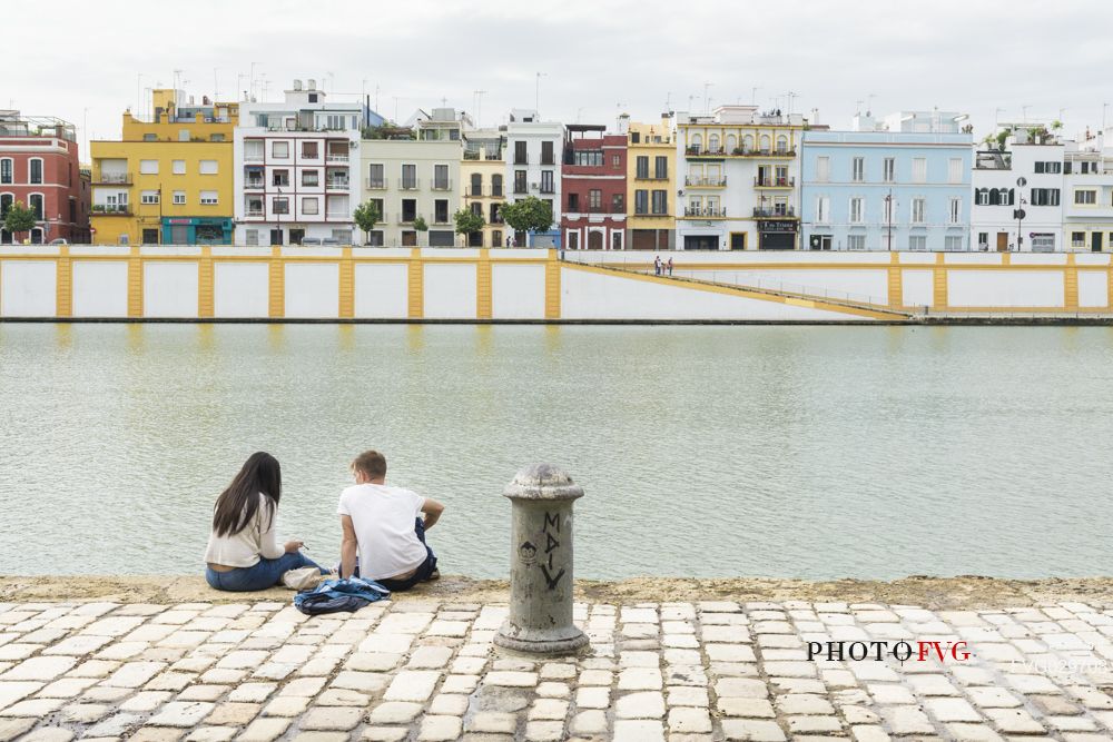 People sitting along the bank of the river Guadalquivir with Triana quarter in the background, Seville, Spain