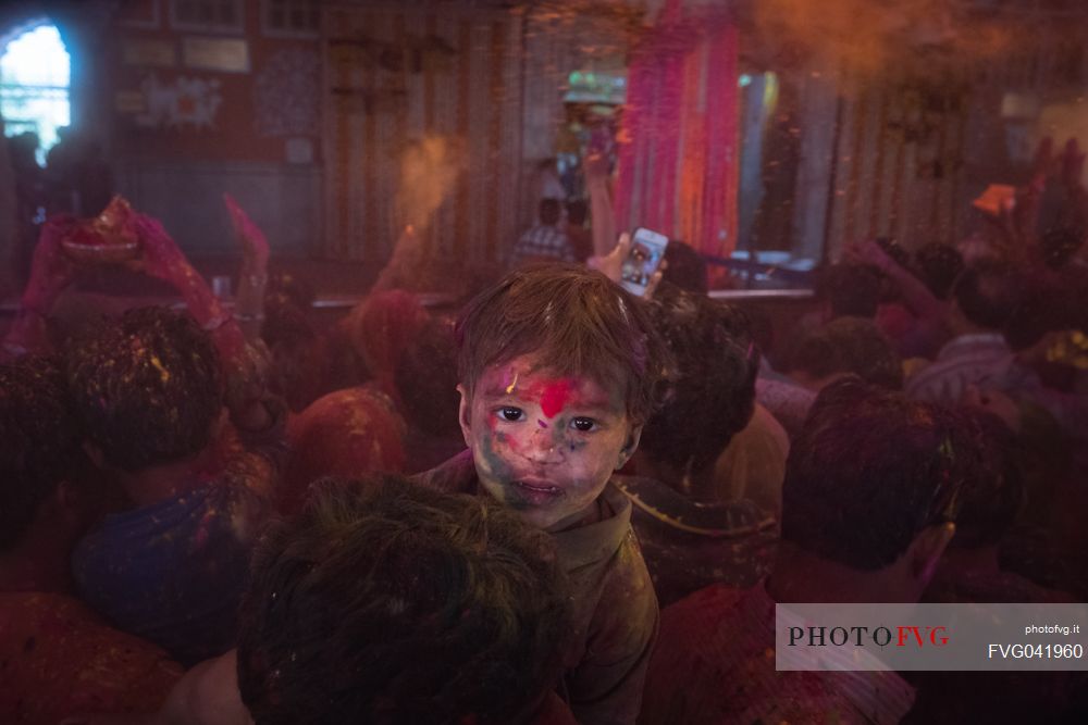 Portrait of a child with colors on his face, during the celebration of holi festival, the festival of colors in a temple in Rajasthan, Jaipur, India