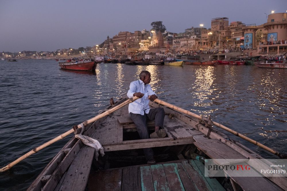Man rowing in his little boat along the river Ganges in Varanasi during sunrise, the city in the background, Uttar Pradesh