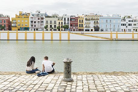 People sitting along the bank of the river Guadalquivir with Triana quarter in the background, Seville, Spain