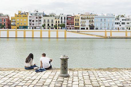 People sitting along the bank of the river Guadalquivir with Triana quarter in the background, Seville, Spain People sitting along the bank of the river Guadalquivir with Triana quarter in the background, Seville, Spain