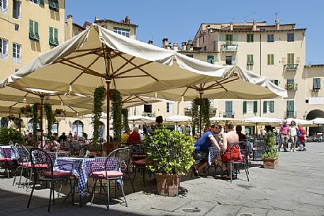 Tourists in the picturesque Piazza Anfiteatro square in Lucca downtown, with its yellow houses and curved walls, Tuscany, Italy