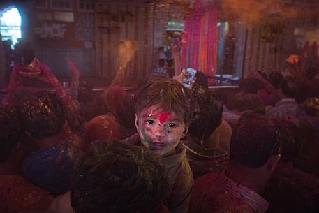 Portrait of a child with colors on his face, during the celebration of holi festival, the festival of colors in a temple in Rajasthan, Jaipur, India