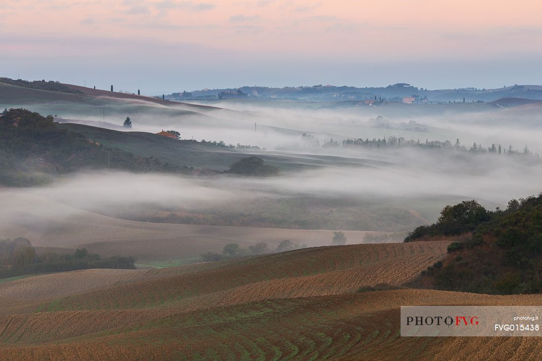 The fog of an autumn sunrise over the hills of Val D'Orcia