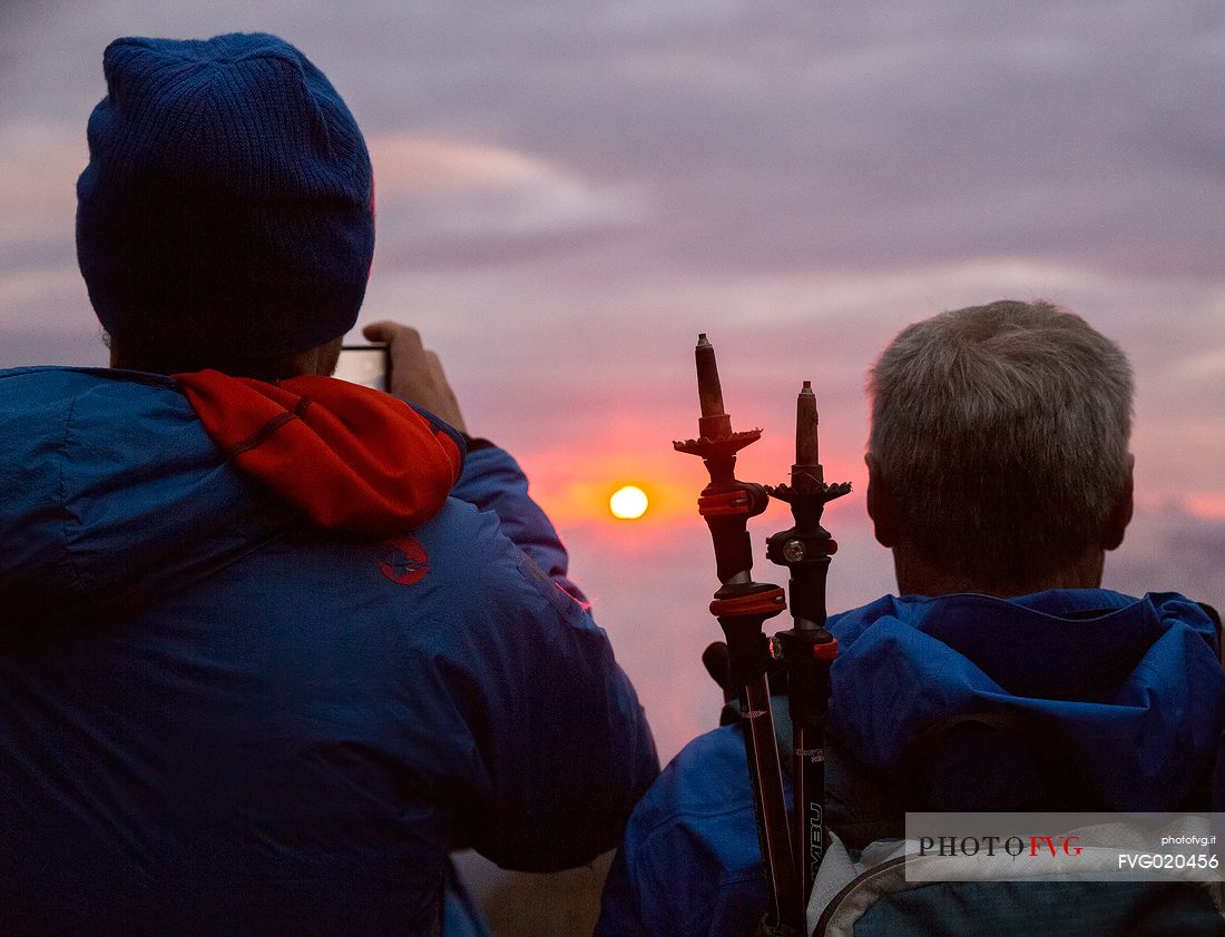 Walkers admire the sunrise from Monte Elmo with the sun rising from the peaks of the Sesto Dolomites