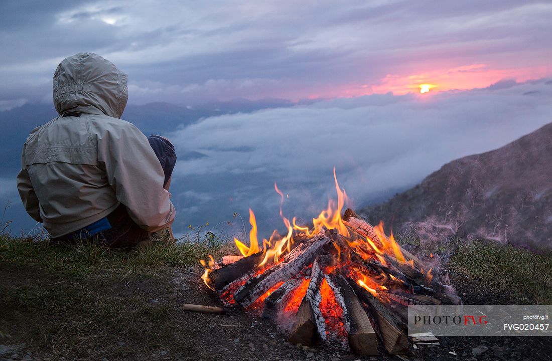 Young trekker can enjoy the sunrise on the Sesto Dolomites from Mount Elmo around a fire