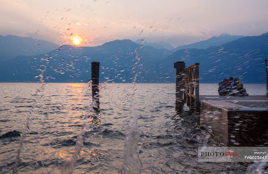 The waves of Lake Garda crash on the shore during a romantic sunset at Malcesine, Italy