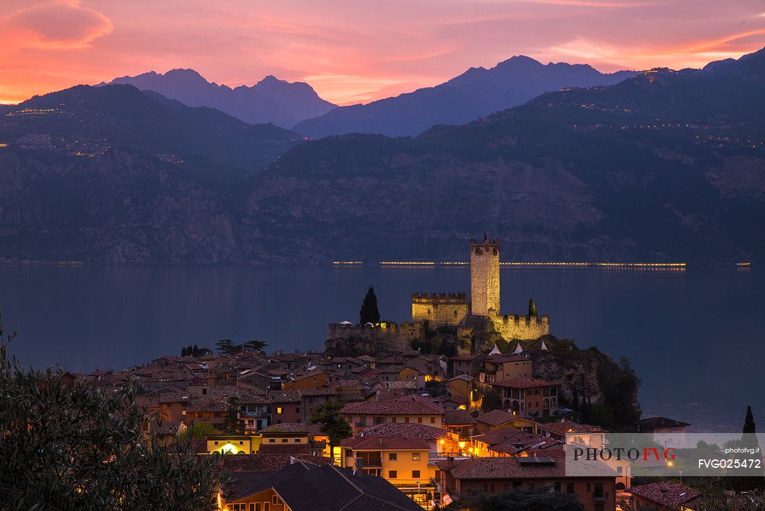 The medieval village and the castle of Scaligero di Malcesine light up soon after a fiery sunset on  Garda lake, Italy