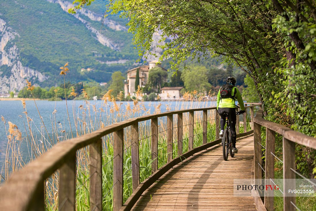 Cyclist along the catwalk of the Toblino lake, on background the Toblino castle, Valley of Lakes, Italy 