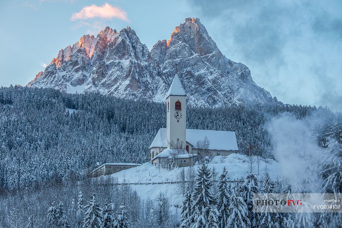 The church of the village of Versciaco after an intense snowfall, in the background the Tre Scarperi peak illuminated at dawn, Innichen, dolomites, Alta Pusteria valley, Trentino Alto Adige, Italy, Europe