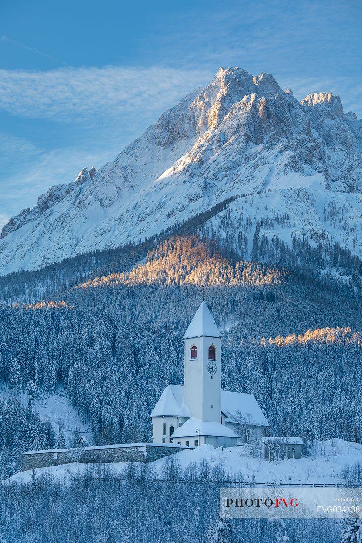 The church of the village of Versciaco after an intense snowfall, in the background the Rocca dei Baranci peak illuminated at dawn, Innichen, dolomites, Pusteria valley, Trentino Alto Adige, Italy, Europe