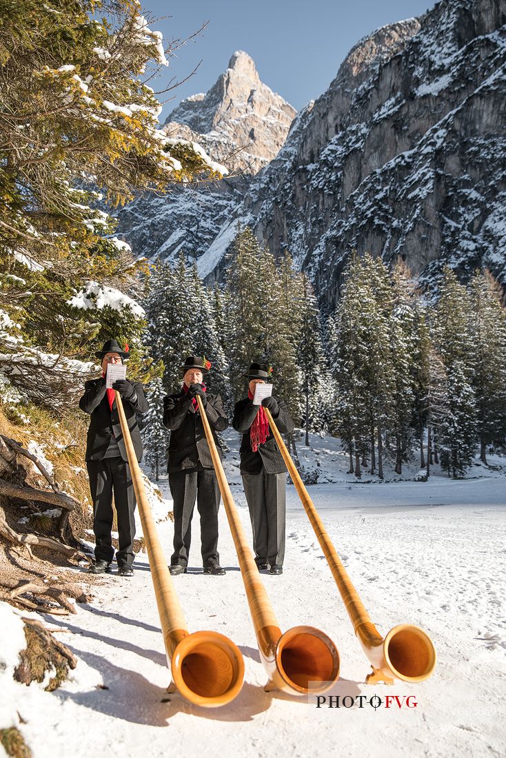 Musicians blowing alphorn on the shore of Braies lake during the Christmas markets of Braies, Pusteria valley, Trentino Alto Adige, Italy, Europe