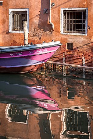  Reflections of a boat and a  Venetian house on the canal in a sunny day