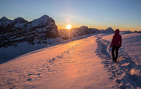 The woman looks at the rising sun , in the background the Tofana di Rozes, the Sorapis and Antelao mount