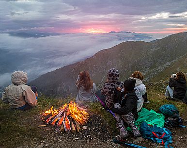 Group of people admire the sunrise on the Sesto Dolomites from Mount Elmo around the fire